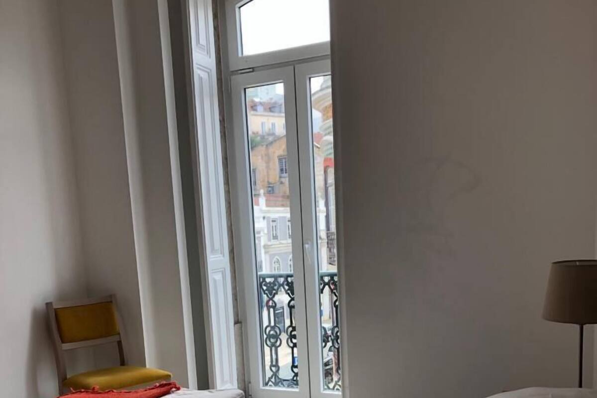 Habitación con dos camas, una silla y ventana con vistas a edificios.