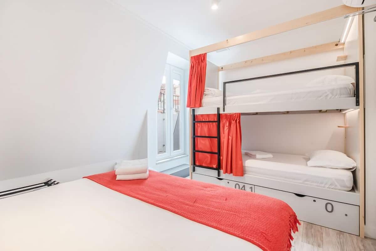 Dormitorio con literas, una manta roja, ropa de cama blanca y un cabecero de madera.