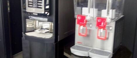 A coffee machine and a vending machine in a room with patterned flooring.