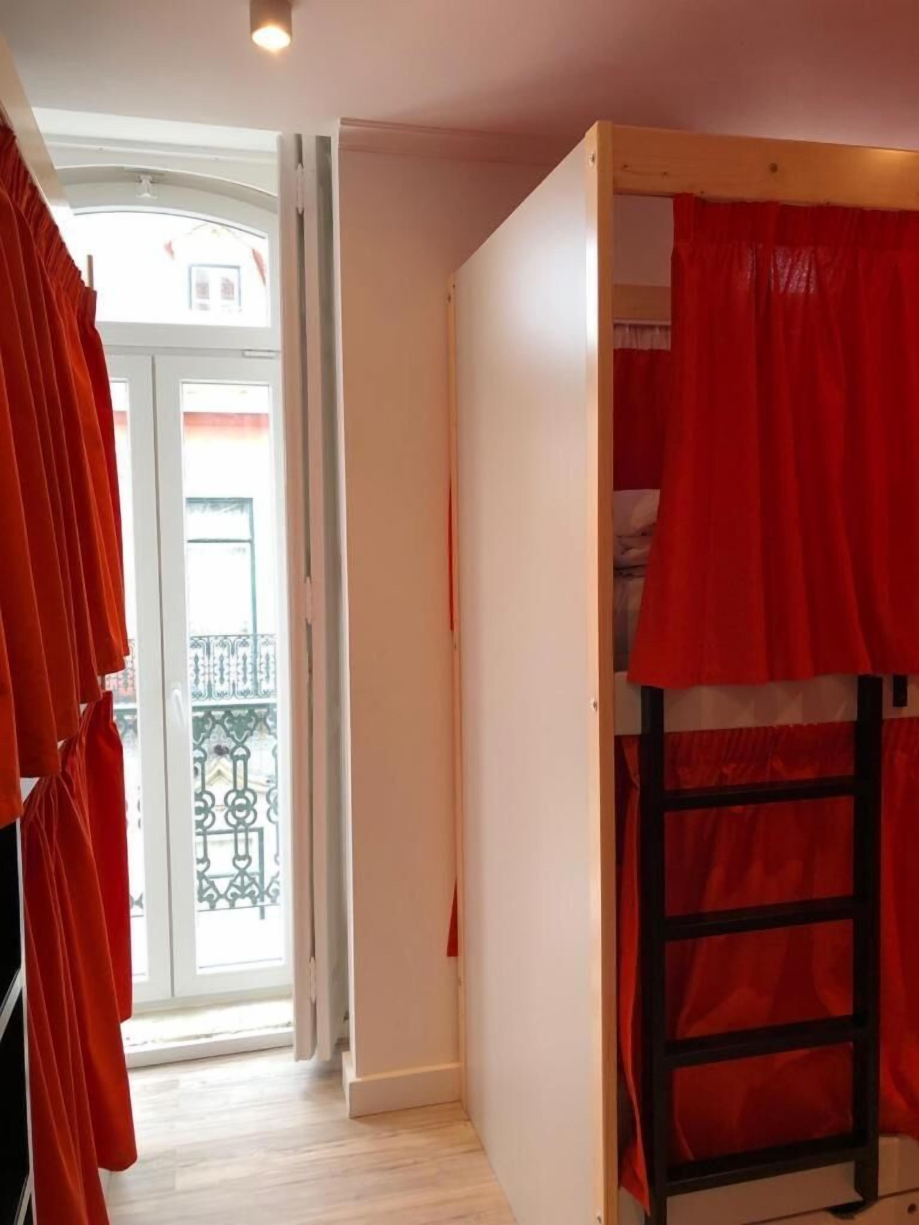 Una habitación con literas, una puerta que da a un balcón exterior y una ventana con cortinas.