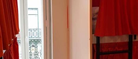 Una habitación con literas, una puerta que da a un balcón exterior y una ventana con cortinas.