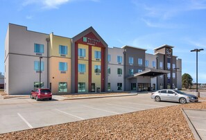 A MainStay Suites hotel with a modern design, featuring a parking lot and a covered entrance.