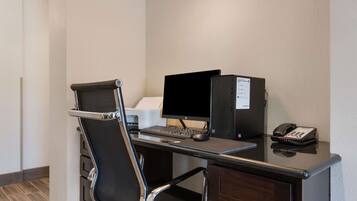 A hotel office with a desk, computer, phone, and a chair.