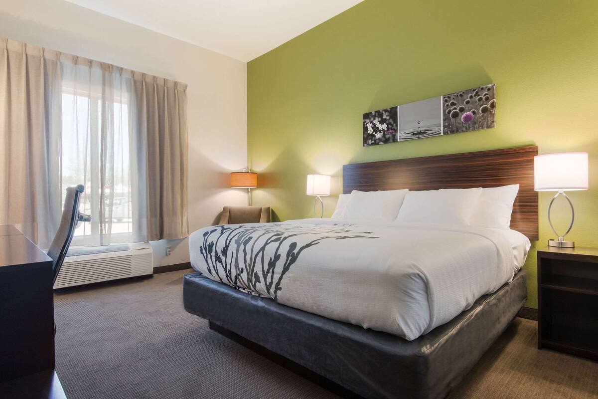 Ett hotellrum med en stor säng, två sängbord med lampor, ett skrivbord och ett fönster med gardiner.