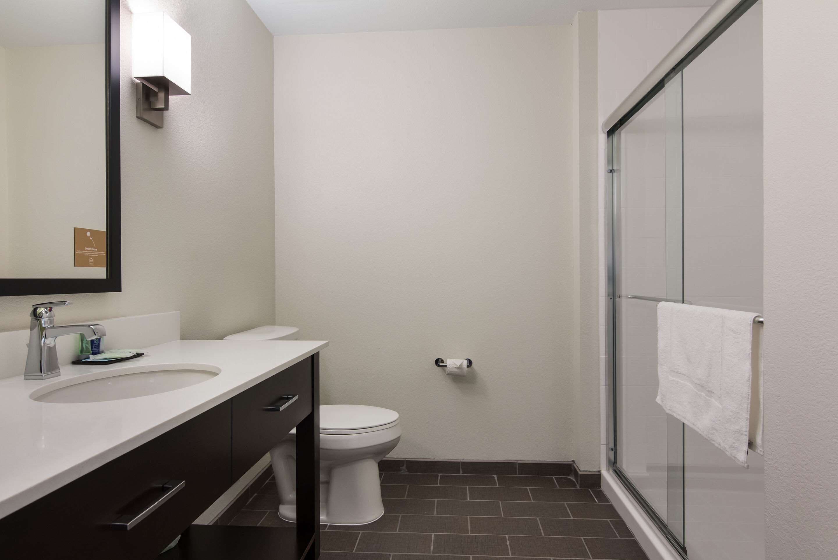 A modern bathroom with a white sink, dark cabinets, a toilet, and a glass shower enclosure.