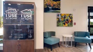 A reception area with a glass display cabinet labeled "THINGS I USE AT HOME," a waterfall painting, and two teal armchairs.
