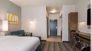 A hotel room with a bed, a desk, a chair, a television, and a door leading to a hallway.
