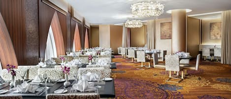 A banquet hall with long tables, patterned chairs, and a chandelier.