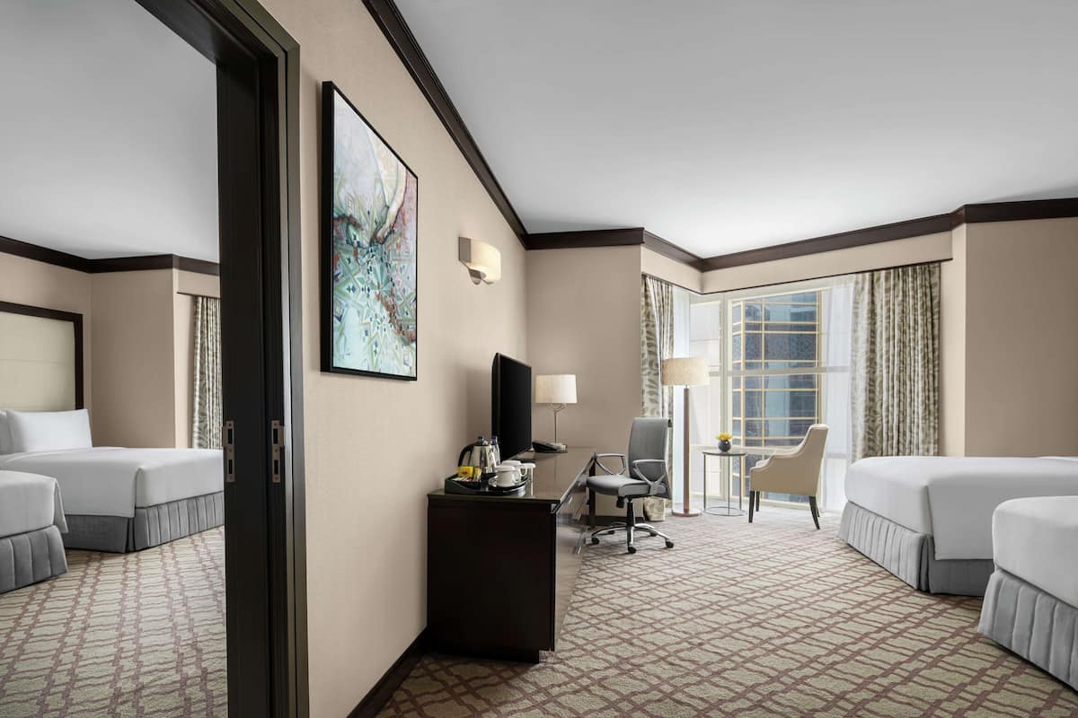 A hotel room with two beds, a desk, a chair, a television, and a large window with curtains.