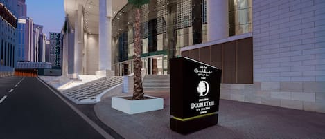 A modern hotel entrance with a curved facade, large columns, and a prominent palm tree sculpture.