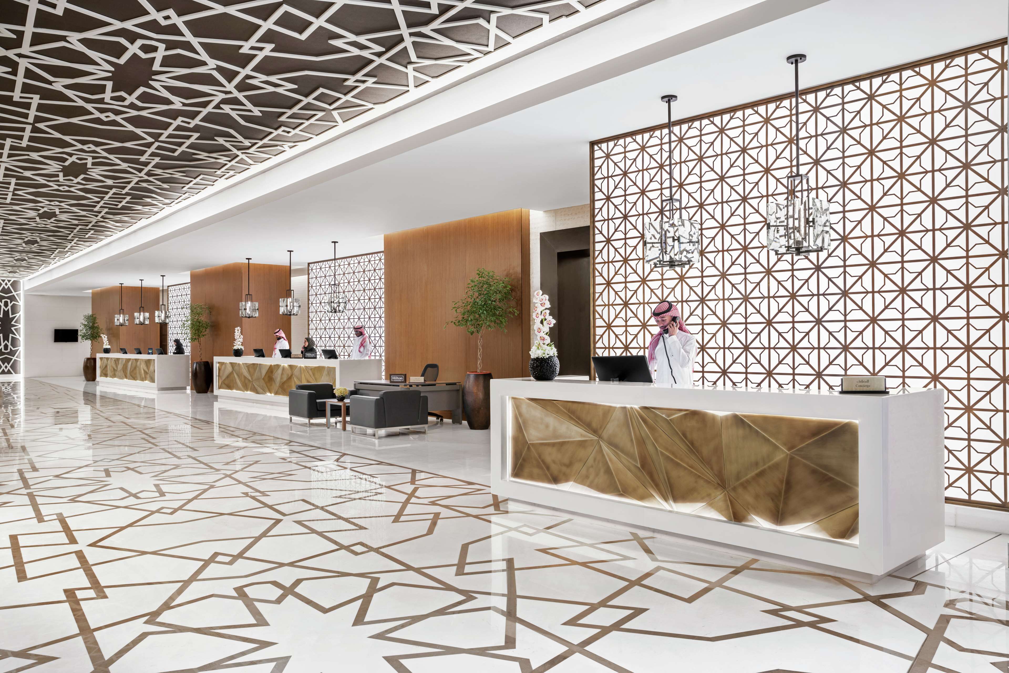 A modern hotel lobby with geometric patterned flooring, reception desks, and decorative lighting.