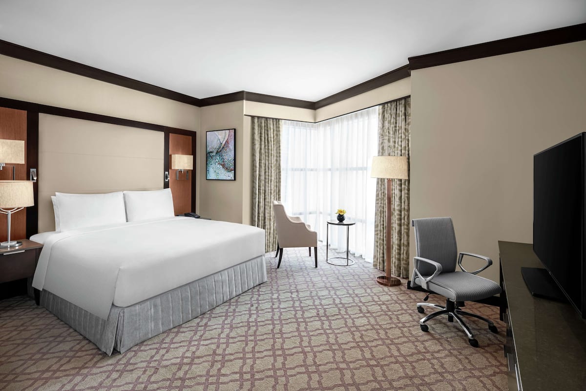 A hotel room with a large bed, a desk with a chair, a TV, and a window with curtains.