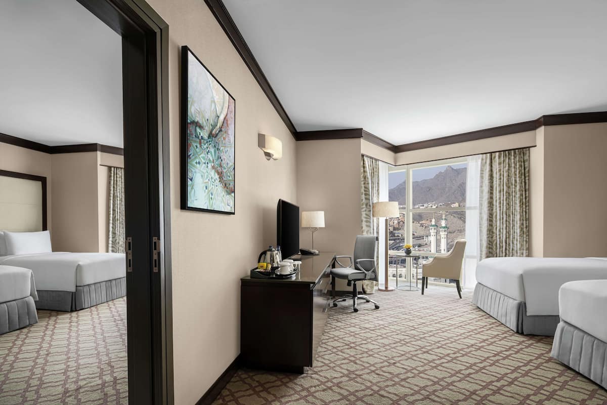A hotel room with two beds, a desk, a chair, a television, and a large window with a city view.