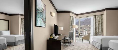 Habitación de hotel con dos camas, un escritorio, una silla, un televisor y un amplio ventanal con vistas a la ciudad.