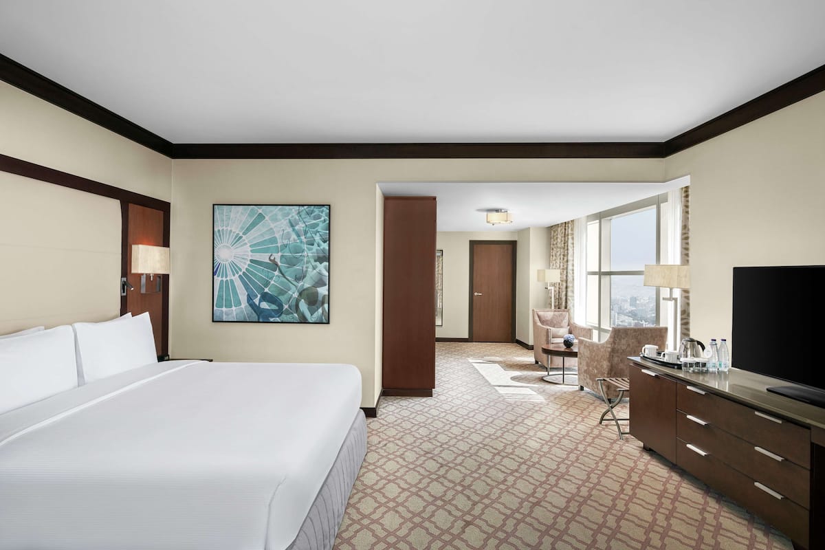 A hotel room with a large bed, a desk with a TV, a chair, and a large window.