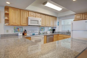 A kitchen with granite countertops, wooden cabinets, a microwave, a stove, a dishwasher, and a refrigerator.