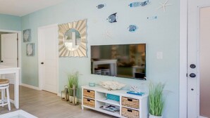 Ein Zimmer mit Fernseher an der Wand, einer weißen Tür, einem weißen Schrank mit Körben und Dekorationselementen wie Seesternen und Muscheln.