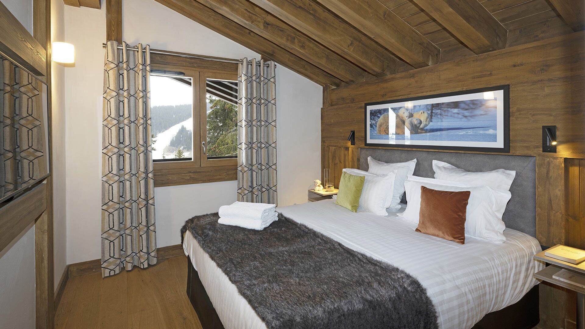 A bedroom with a large bed, wooden ceiling beams, a window with a view of trees, and a framed picture on the wall.