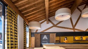 A modern hotel lobby with a wooden ceiling, large windows with checkered curtains, a reception desk, and a sign for 'A MAYA'. - MGM Hôtels & Résidences – Résidence Amaya (Villard-sur-Doron)