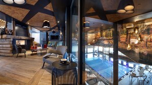 A modern interior with a fireplace, seating area, and a glass-enclosed pool with a forest mural. - MGM Hôtels & Résidences – Résidence Amaya (Villard-sur-Doron)