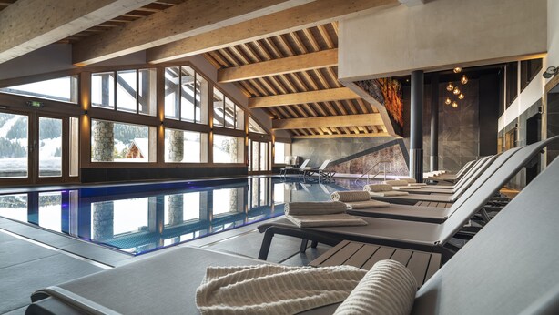 A modern indoor pool area with sun loungers and a view of a snowy landscape through large windows. - MGM Hôtels & Résidences – Résidence Amaya (Villard-sur-Doron)