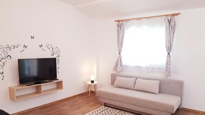 Uma sala de estar moderna com televisão de tela plana, um sofá, uma pequena mesa lateral com luminária e um tapete estampado.