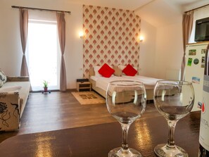 Una habitación con cama, una mesita con dos vasos, un sofá y una ventana con cortinas.