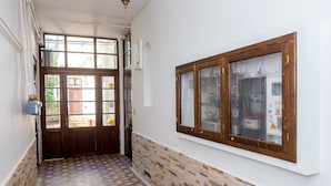 Um corredor com ladrilhos estampados, uma porta de madeira e uma janela embutida na parede, com moldura de madeira.