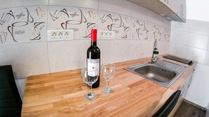 Uma cozinha com bancada de madeira, uma garrafa de vinho, duas taças de vinho, uma pia e uma parede com ilustrações de xícaras de café.