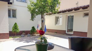Um pátio com uma mesa, uma cadeira, um vaso de planta e um edifício com bandeiras.