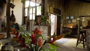 Une pièce rustique avec une cheminée en pierre, des poutres en bois et des plantes tropicales.