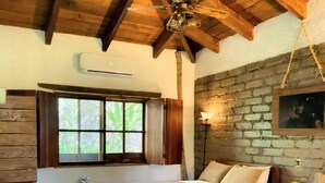 Une chambre avec deux lits, des poutres en bois, un mur en briques et une fenêtre avec des rideaux.