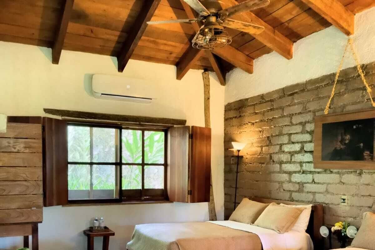 Ein Zimmer mit zwei Betten, Holzbalken, einer Ziegelwand und einem Fenster mit Vorhängen.