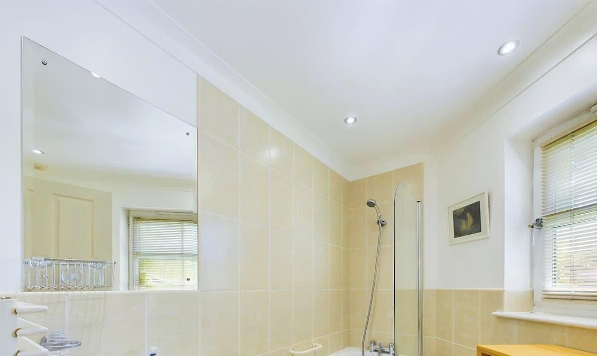 Een badkamer met een grote spiegel, douche, wastafel en een raam met jaloezieën.