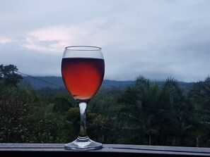 Una copa de vino tinto en un balcón con vistas a un paisaje montañoso y vegetación.