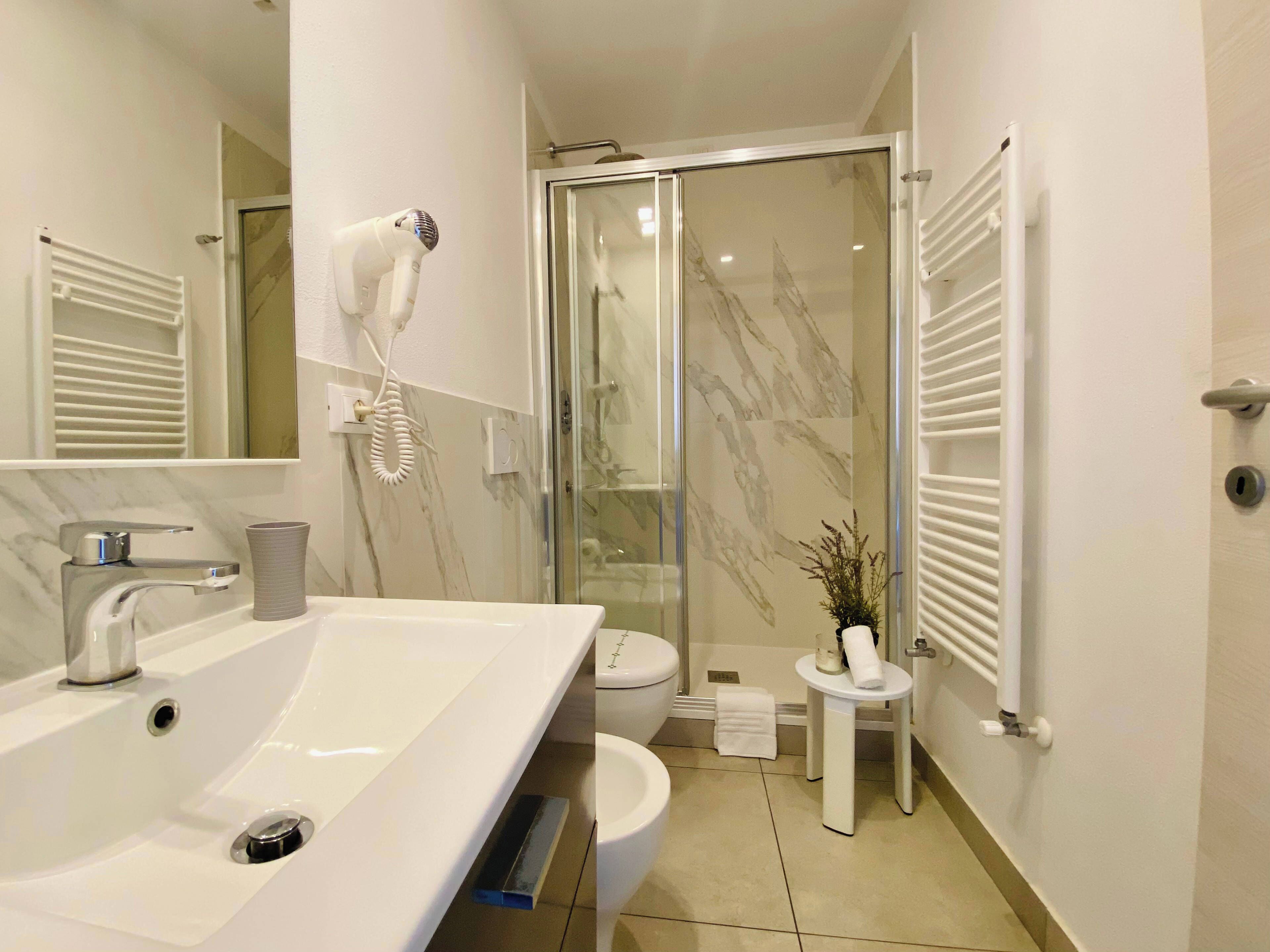 Ein modernes Badezimmer mit einem großen Waschbecken, einem Föhn, einer Toilette und einer Duschkabine aus Glas.