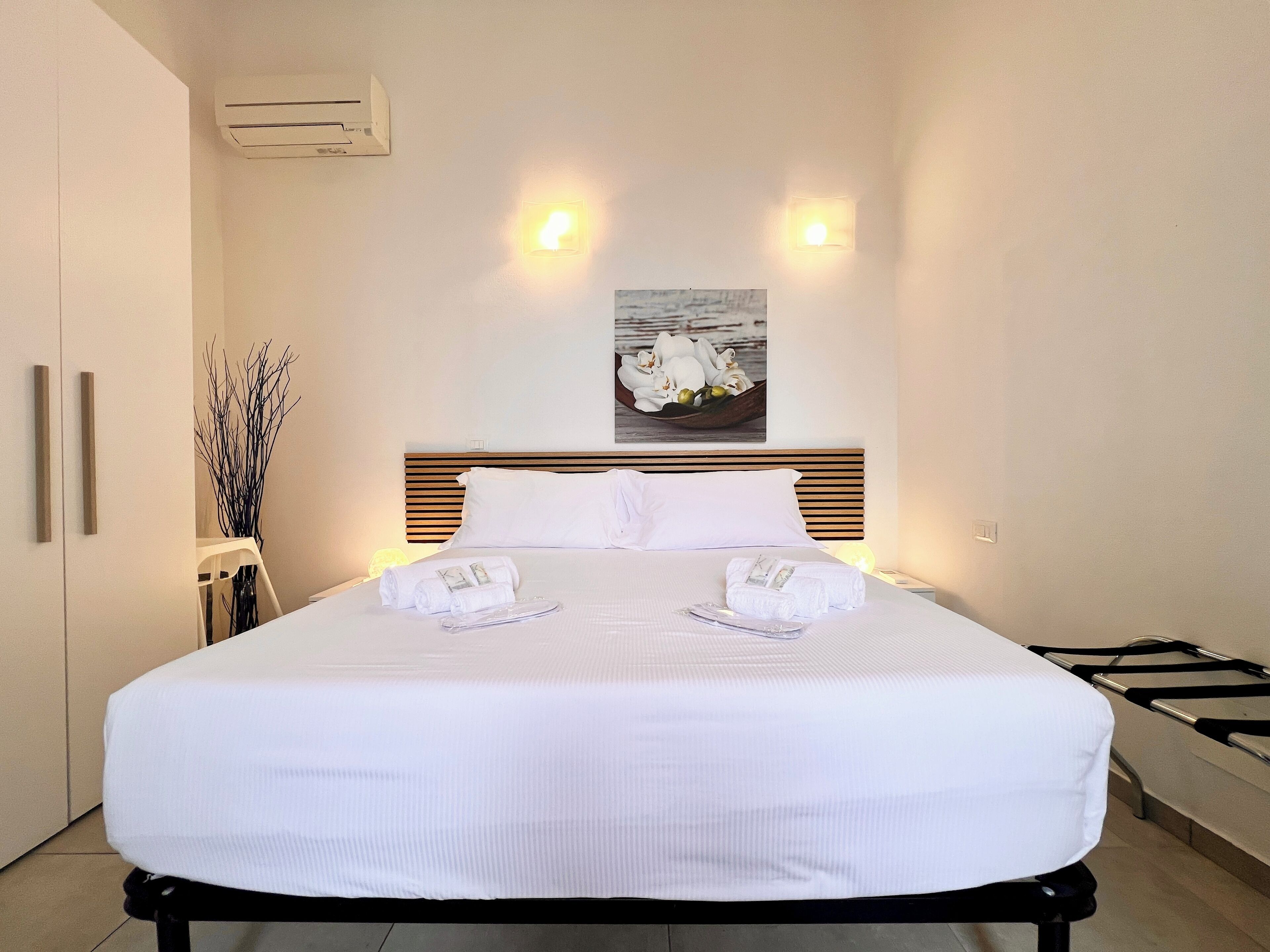 A neatly made bed with white linens and towels, a wooden headboard, and a wall-mounted air conditioner.