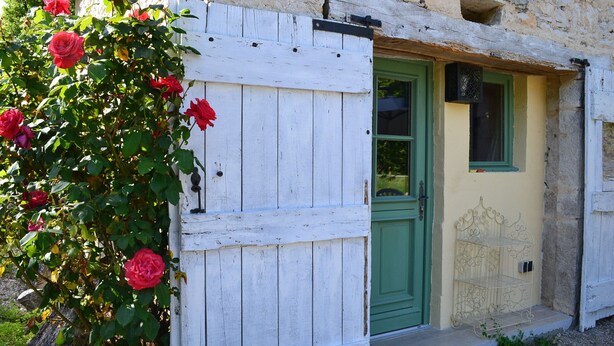 A rustic building with a white wooden door and green shutters, a small balcony with a metal railing, and a garden with red roses. - Couanac, cottage in the countryside with swimming pool (Cayriech)