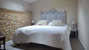 A bedroom with a stone wall, a wooden bed with white bedding, and two bedside lamps. - Couanac, cottage in the countryside with swimming pool (Cayriech)