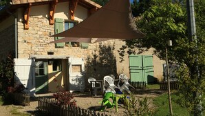 A stone house with a sloped roof, green shutters, and a patio area with outdoor furniture. - Couanac, cottage in the countryside with swimming pool (Cayriech)