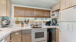 A kitchen with a stove, microwave, and refrigerator, wooden cabinets, and a window with blinds.