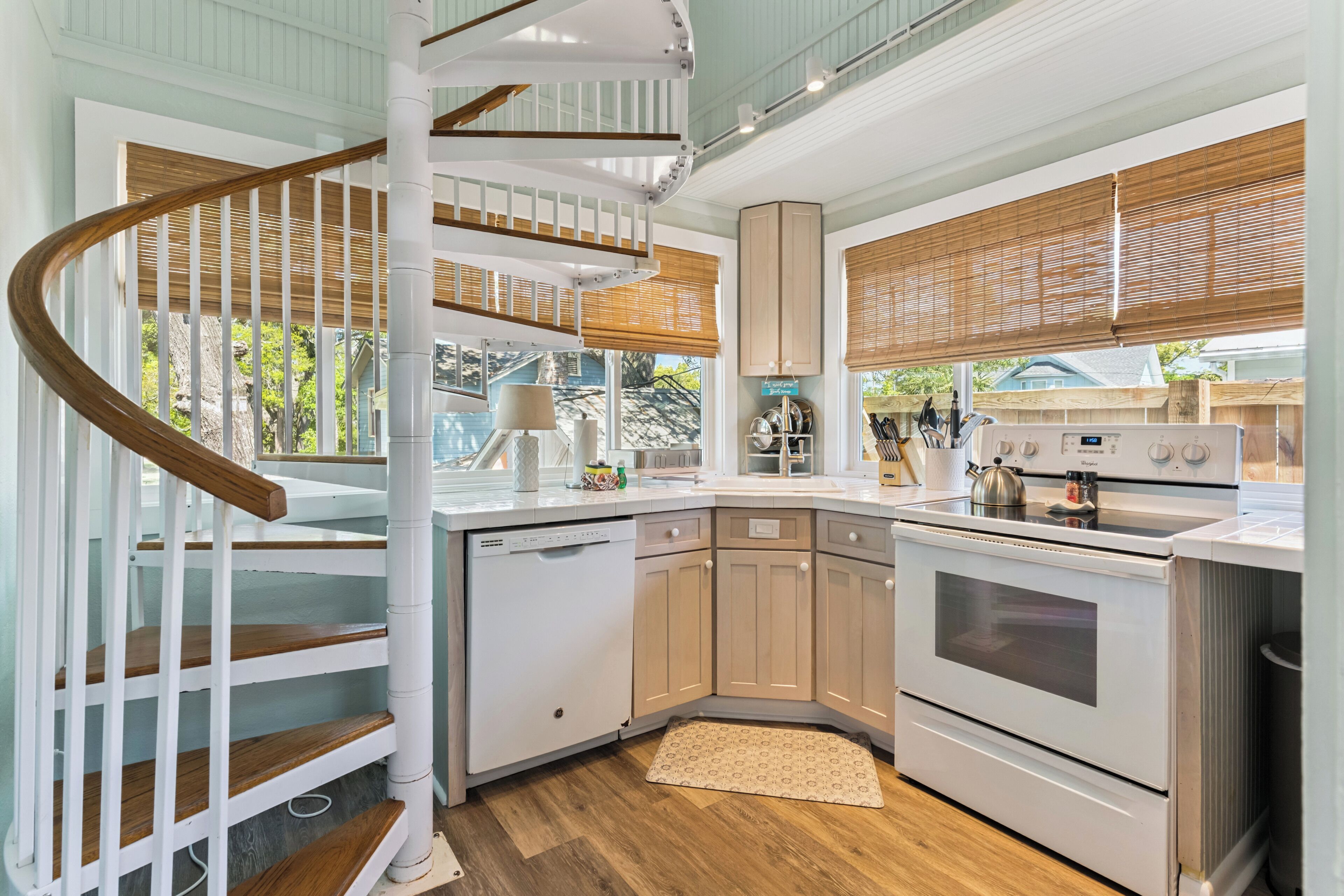 Une cuisine avec un escalier en colimaçon blanc, des meubles de rangement en bois, une cuisinière et un lave-vaisselle.
