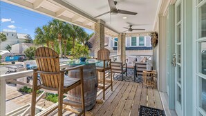 A covered outdoor area with wooden chairs, a glass-top table, and a ceiling fan.