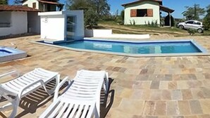 Zona de piscina con jacuzzi, sillas de descanso y una pequeña casa al fondo.