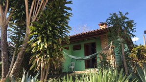 Una casa con fachada verde, techo de tejas rojas y una hamaca en el jardín.