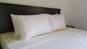 Un letto rifatto con lenzuola e cuscini bianchi, una testata scura e una parete spoglia.