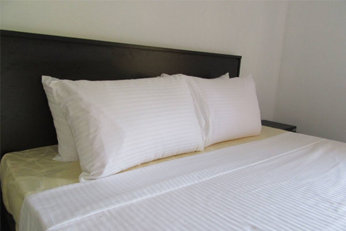 Una cama bien hecha con sábanas y almohadas blancas, un cabecero oscuro y una pared lisa.