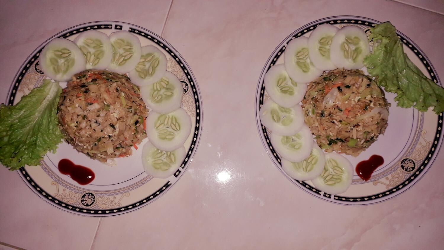 Two plates of food with lettuce and cucumber slices, and a heart-shaped sauce on a tiled surface.