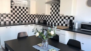 Une cuisine moderne avec des armoires blanches, un crédence à carreaux noirs et blancs, une hotte de cuisinière en acier inoxydable et une table à manger avec des chaises.