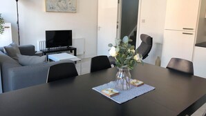 Un salon moderne avec une table à manger noire, un canapé gris et un téléviseur posé sur un meuble.